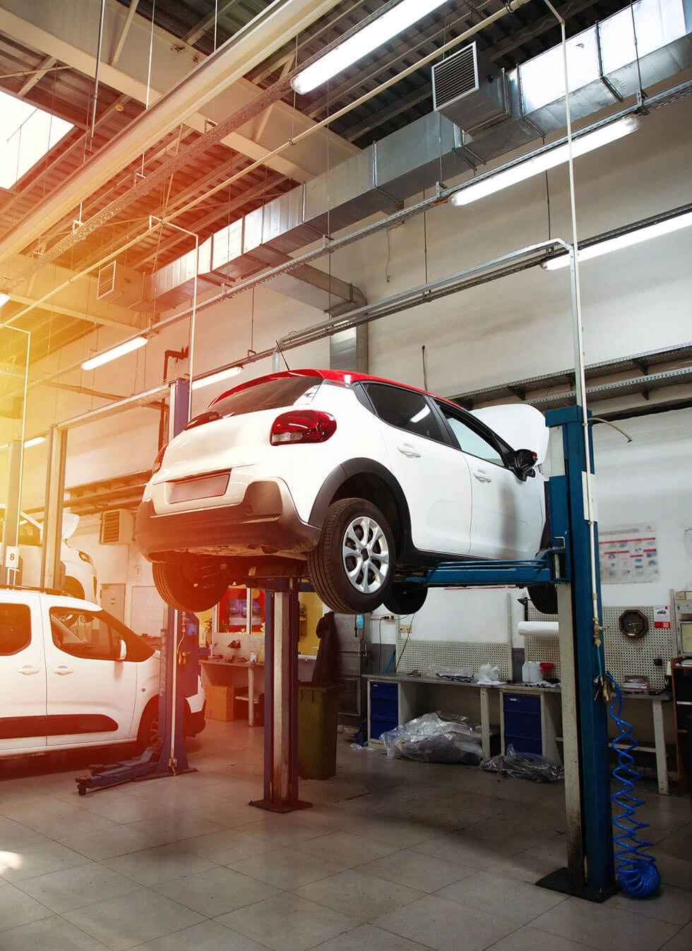 A white hatchback vehicle raised on a hydraulic lift inside a modern auto repair service bay.